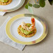 A Visions white plastic plate with a gold lattice design holding shrimp and avocado.