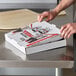 A person opening a Choice white corrugated pizza box on a table.