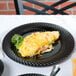 A Visions Wave black plastic plate with an omelet on a table.