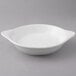 A Tuxton white round china shirred egg dish with a handle on a gray surface.