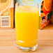 A Libbey Cascade beverage glass filled with orange juice on a table in a juice bar.