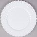 A white Fineline Flairware plastic plate with a scalloped edge on a gray surface.