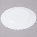 A white Fineline Flairware plastic plate with scalloped edges on a white surface.