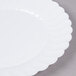 A close up of a white Fineline Flairware plastic plate with scalloped edges.