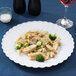 A Fineline white plastic plate with pasta, broccoli, and chicken.