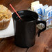A black Visions plastic coffee mug filled with coffee on a table with a muffin.