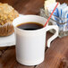 A Visions plastic coffee mug filled with coffee and a straw next to a muffin.