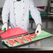 A chef cutting raw meat on a green Choice steak paper-covered cutting board.