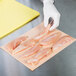A person in white gloves using a piece of 9" x 12" LitePeachTreat steak paper to hold raw chicken meat.