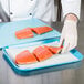 A person in a white coat cutting raw salmon on a blue cutting board.