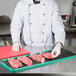 A chef using a knife to cut raw meat on a black steak paper sheet.