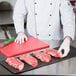 A chef using a knife to cut raw meat on a red cutting board.