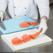 A chef cutting raw salmon on a white surface with a knife.