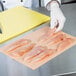 A person using LitePeachTreat steak paper to wrap raw chicken breasts on a cutting board.