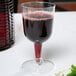 A Visions clear plastic wine goblet filled with red wine on a table.
