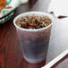 A Dart translucent plastic cup filled with ice and soda on a table.