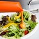 A bowl of salad with orange sauce being poured into it using a Carlisle PourPlus spout.