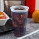 A Dart translucent plastic cup with ice and liquid on a tray with a hamburger and an orange.
