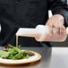 A person pouring liquid from a Carlisle Store 'N Pour container into a salad.