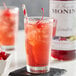 A glass of pink liquid with ice and a straw made with Monin Premium Grenadine syrup.