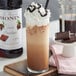 A glass of Monin Swiss chocolate flavoring syrup with whipped cream and chocolate on top.