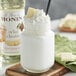 A glass jar of white Monin Premium White Chocolate flavoring syrup with a straw in it.
