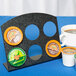 A black Cal-Mil coffee pod holder with round holes holding coffee pods over a cup of coffee.