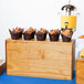 A Cal-Mil rustic pine rectangle plate riser holding a group of muffins on a table outdoors.