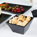 A black square Cal-Mil melamine bowl with crackers and olives.