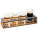 A Cal-Mil Madera rustic pine wooden tasting flight with four glasses of beer on a table.