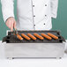 A chef uses tongs to cook hot dogs on a Cal-Mil cast iron grill.