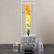 A clear plastic Cal-Mil beverage dispenser with fruit in the infusion chamber.