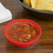 A red bowl of salsa on a table with a bowl of chips.