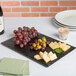A rectangular faux slate Cal-Mil serving platter with cheese and grapes on a table.