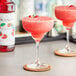 Two glasses of pink strawberry margaritas on a table with a bottle of Monin Premium Strawberry Flavoring.