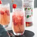 A glass of Monin raspberry drink with a straw and raspberry on top.