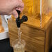 A hand pouring water from a Cal-Mil Madera Rustic Pine beverage dispenser into a glass.