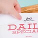 A hand holding a paper with the words "daily special" on a wood display stand with the Cal-Mil Madera Displayette.