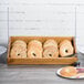 A Madera rustic pine display bin with bagels and bowls on a table.