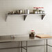 A Regency stainless steel wall shelf above a counter in a professional kitchen.