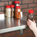 A hand holding a jar of spices on a Regency stainless steel wall shelf.