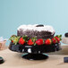A black Elite Global Solutions ruffled edge melamine cake stand with a cake topped with strawberries.