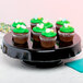 A black Elite Global Solutions ruffled edge melamine cake stand with a cupcake with green frosting and candy on top.