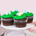 A hand holding an Elite Global Solutions white melamine plate with chocolate cupcakes with green frosting and candy eggs.
