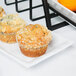 A white rectangular melamine tray with three muffins on it next to an orange.