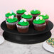 An Elite Global Solutions black melamine pedestal with cupcakes with green frosting and candy eggs on top.