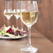 A close-up of a Spiegelau white wine glass filled with white wine on a table with salad.