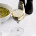 A Spiegelau Authentis wine glass filled with white wine next to a bowl of soup.