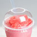 A Dart clear plastic dome lid with a straw hole on a plastic cup with a pink drink.