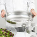 A chef holding a Vollrath stainless steel water pan filled with salad.